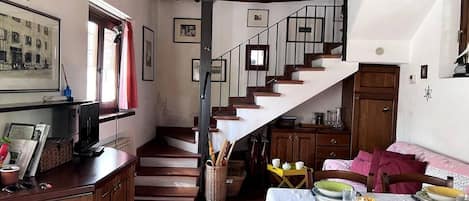 Um interior acolhedor com uma escada que leva a uma área de refeições, armários de madeira e uma televisão em uma prateleira.