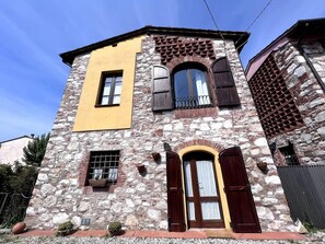 A stone building with a yellow facade, a wooden door, and a window with shutters. - Casa Silvia a piedi dalle mura AC (LUCCA)