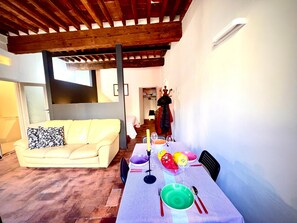 A dining area with a table set for two, a sofa, and a coat rack with a coat and hat. - civico 12 appartamento in centro storico (LUCCA)