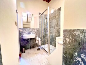 A bathroom with a glass shower enclosure, a sink, and a mirror. - civico 12 appartamento in centro storico (LUCCA)