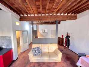 A living room with a beige sofa, a wooden ceiling, a staircase, and a red chair. - civico 12 appartamento in centro storico (LUCCA)