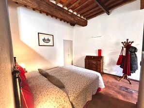 A bedroom with a bed, a wooden wardrobe, a coat rack, and a door. - civico 12 appartamento in centro storico (LUCCA)