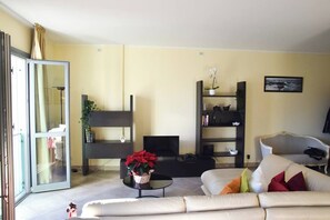 A living room with a sofa, a coffee table with a flower vase, a TV, and a bookshelf. - Casa ai giardini in front of the ancient wall (LUCCA)