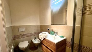 Een badkamer met toilet, bidet, wastafel met spiegel en een douchehoek.