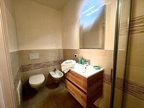 Casa de banho com sanita, bidé, toucador com espelho e zona de duche.
