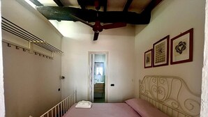 Een slaapkamer met een bed, een kledingkast, een plafondventilator en een deur naar een trap.