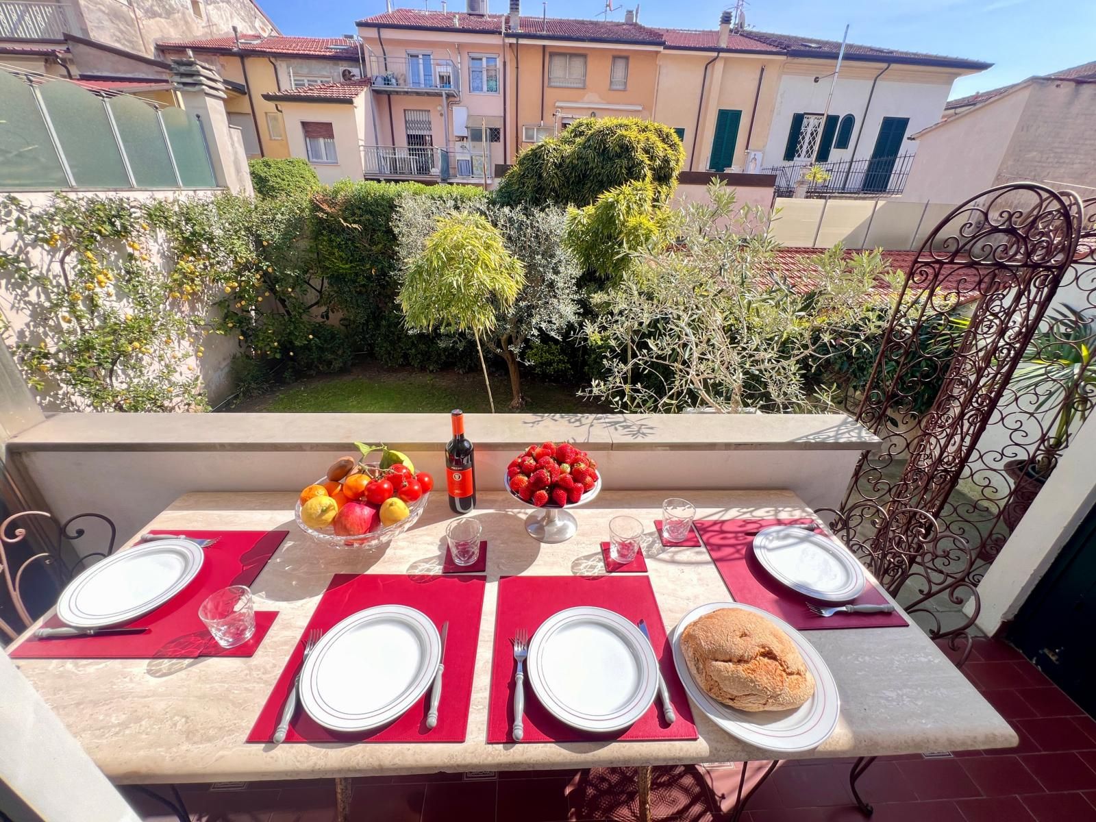 Una terraza con una mesa dispuesta para dos personas, que incluye una botella de vino, fruta y pan.