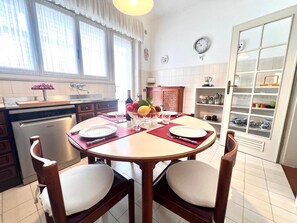 Una cocina con una mesa redonda de comedor, sillas, un lavavajillas y un armario con vajilla.
