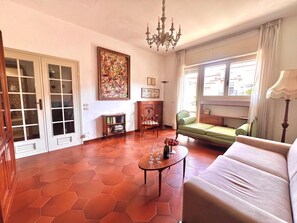 Ein Wohnzimmer mit einer Couch, einem Couchtisch, einem Bücherregal, einem Gemälde und einem Fenster mit Vorhängen.