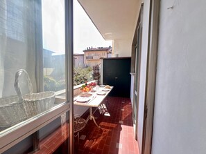 Un balcón con una mesa de comedor lista para dos personas, una silla de mimbre y vistas de edificios vecinos.