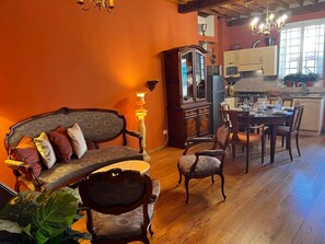 A room with a wooden floor, a dining table set for four, a sofa with cushions, and a cabinet with glass doors. - Casa Florian in the historic center (LUCCA)