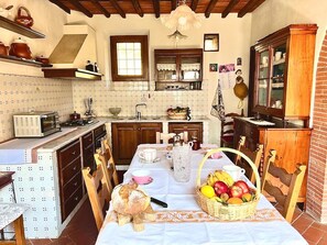 Cozinha com mesa posta para o café da manhã, com uma cesta de frutas e uma chaleira.