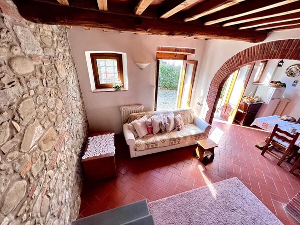 Um quarto aconchegante com parede de pedra, um sofá, uma mesinha e uma janela.