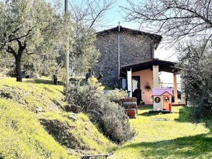 Um edifício de pedra com uma pequena construção anexa, rodeado por vegetação e árvores.