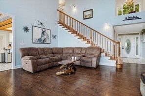 A spacious living room with a large sectional sofa, a wooden coffee table, and a staircase with wooden railings. - New Listing, Hot Tub, Arcade Games, Free Attractions, Mountain Views (Gatlinburg)