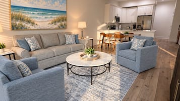 A modern living room with a sofa, armchairs, a coffee table, and a painting of a beach scene.