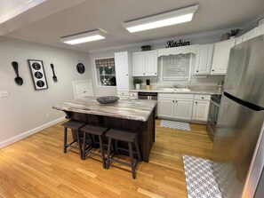 A modern kitchen with white cabinets, a marble island, and a stainless steel refrigerator. - River Bend | Riverfront Views, Hot Tub & Game Room (Ellijay)