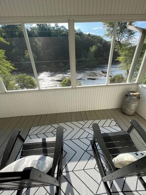 A covered porch with two rocking chairs, a metal trash can, and a view of a river. - River Bend | Riverfront Views, Hot Tub & Game Room (Ellijay)