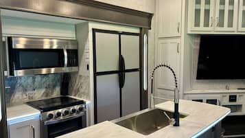 A modern kitchen with stainless steel appliances, a built-in microwave, a double-door refrigerator, and a curved sink.