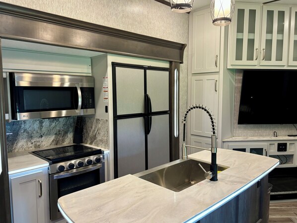 Una cocina moderna con electrodomésticos de acero inoxidable, microondas integrado, refrigerador de doble puerta y un lavamanos curvo.