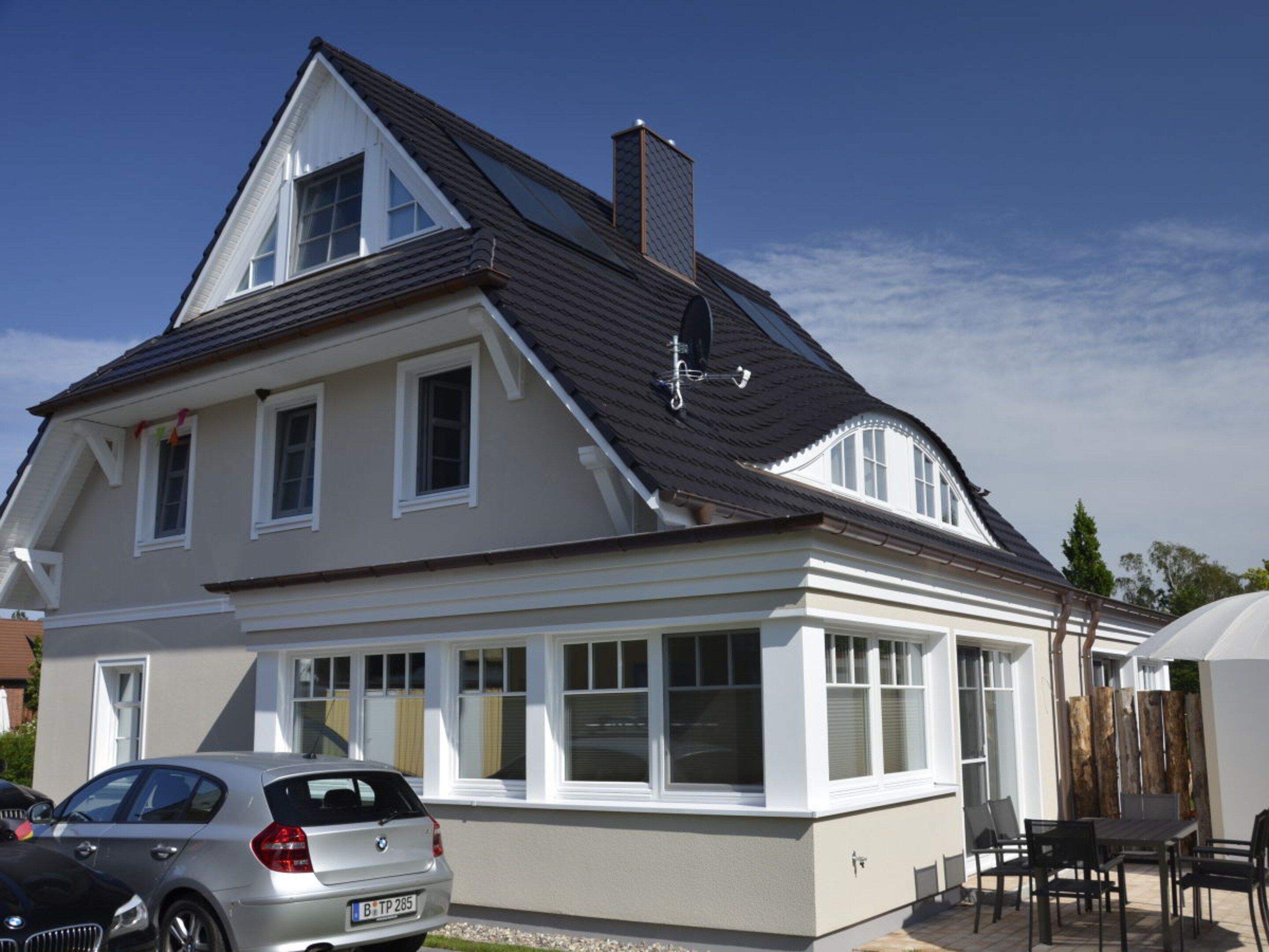 A two-story house with a sloped roof, large windows, and a car parked in the driveway.