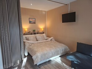 A bedroom with a bed, bedside lamps, a flat-screen TV, and a sofa.