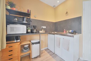 A compact kitchen with a microwave, coffee maker, and a small trash bin.