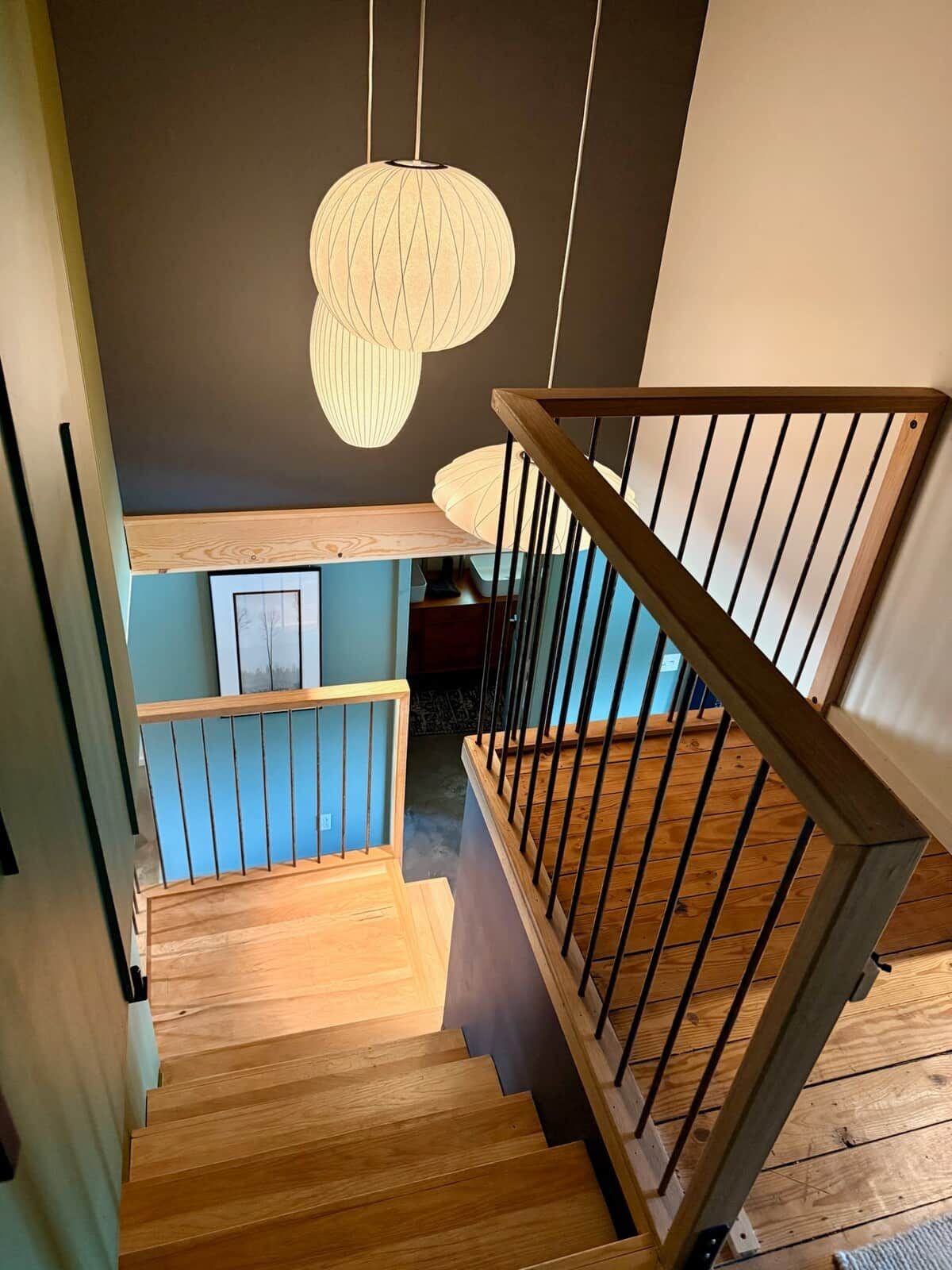 A wooden staircase with a railing, leading to a lower level with a blue wall and framed artwork.