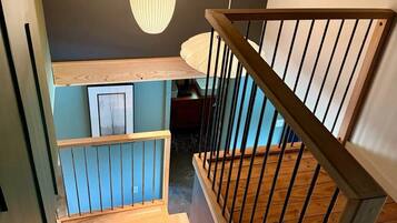A wooden staircase with a railing, leading to a lower level with a blue wall and framed artwork.