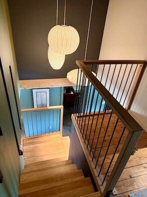 A wooden staircase with a railing, leading to a lower level with a blue wall and framed artwork. - Raven Cove: 5BR Lakefront Home w/ Private Hot Tub (Mina)