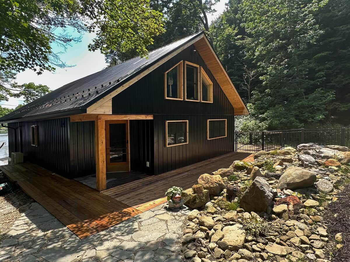 A cabin with a wooden deck, a large window, and a stone pathway.