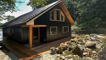 A cabin with a wooden deck, a large window, and a stone pathway.