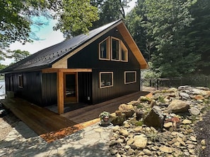 A cabin with a wooden deck, a large window, and a stone pathway. - Raven Cove: 5BR Lakefront Home w/ Private Hot Tub (Mina)