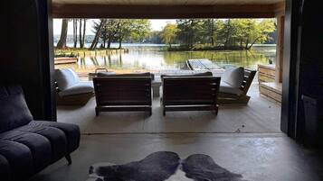 A room with a large window overlooking a lake, two wooden benches, a sofa, and a rug.