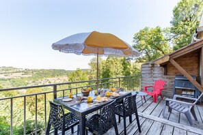 A deck with a table set for dining, outdoor chairs, a grill, and a view of the countryside. - L’Échappée Belle - joli appt avec piscine partagée (Caylus)