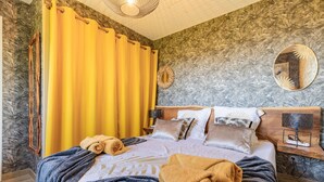 Une chambre d’hôtel avec un lit, une tête de lit en bois, un miroir, une table de chevet et un rideau jaune.