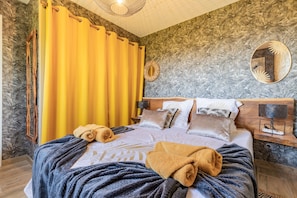 A hotel room with a bed, a wooden headboard, a mirror, a nightstand, and a yellow curtain. - L’Échappée Belle - joli appt avec piscine partagée (Caylus)