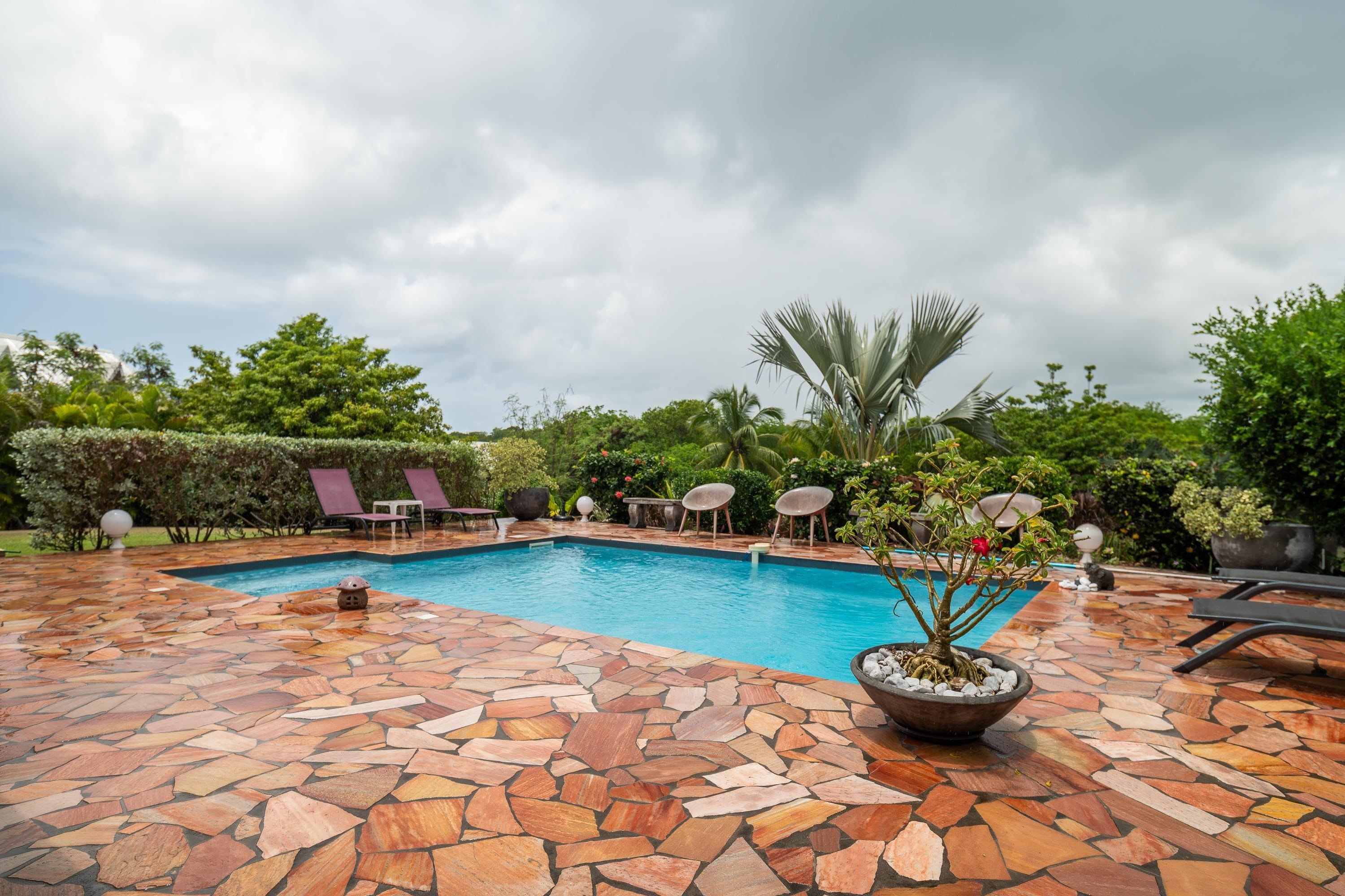 A swimming pool with stone flooring, surrounded by lounge chairs and potted plants.