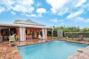 A swimming pool with a tiled deck, outdoor furniture, and a covered patio area. - Villa Devaki - Piscine Privée (Saint-Francois)