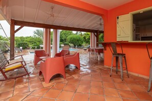 A covered outdoor area with a pool, red chairs, and a bar area. - Villa Devaki - Piscine Privée (Saint-Francois)