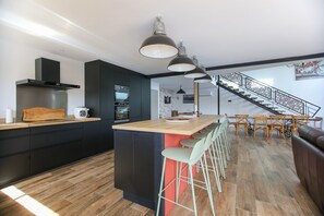 A modern kitchen with a central island, bar stools, and a staircase leading to a dining area. - L'entre'Potes - Piscine Privée (Nalliers)