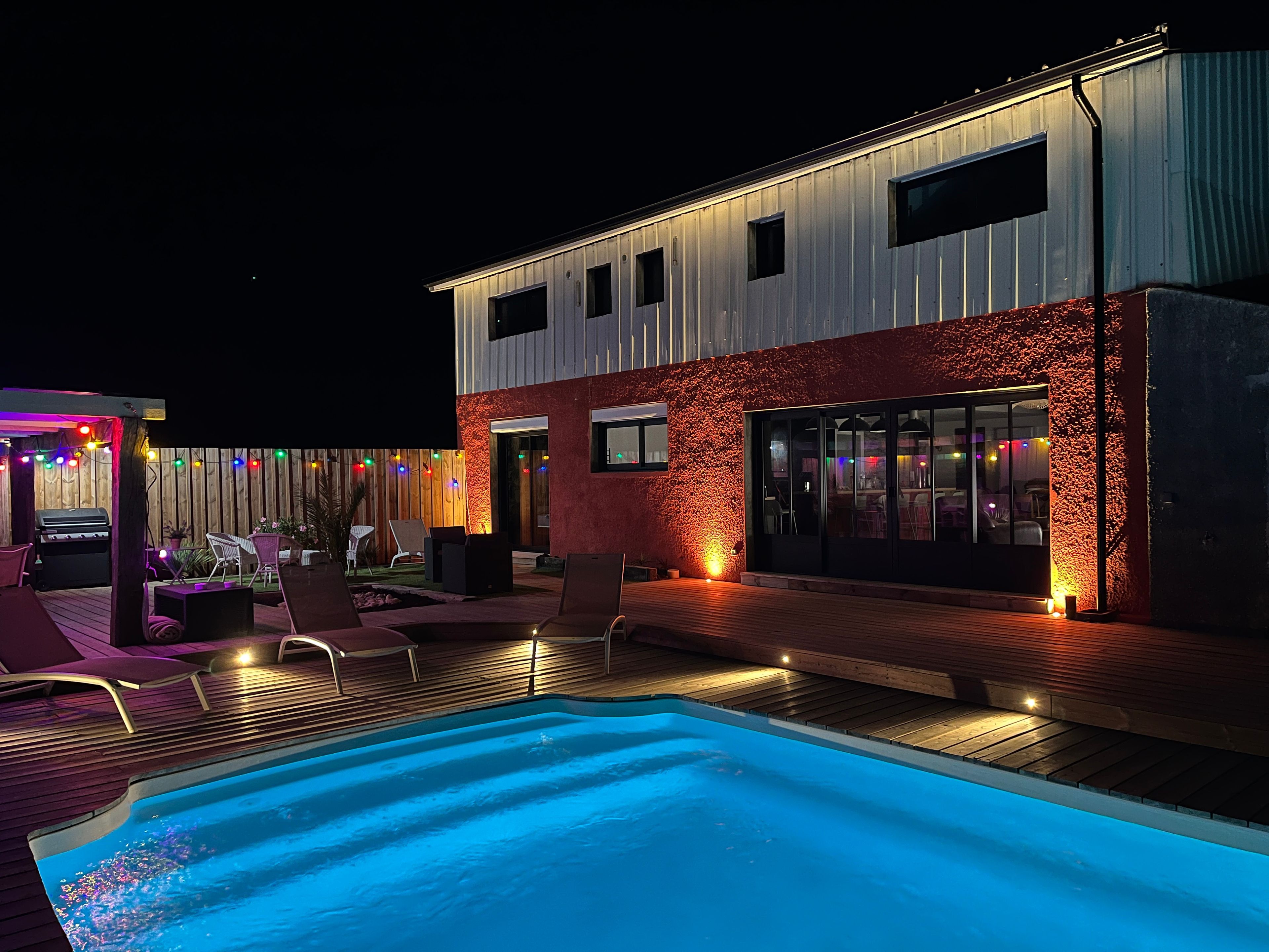 Un espace piscine extérieur moderne, doté d’une terrasse en bois, de chaises longues et d’un barbecue.