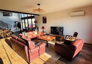 A spacious living room with leather sofas, a wooden coffee table, and a television. - L'entre'Potes - Piscine Privée (Nalliers)