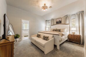 A bedroom with a bed, a sofa, a bedside table, a lamp, a mirror, a window with curtains, and a ceiling light. - The Well Spoke Inn | Bike to Downtown + Coler (Bentonville)