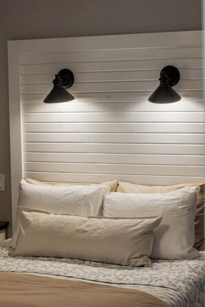 A bed with a headboard against a wall, two wall-mounted lamps, and a floral-patterned bedspread. - The Well Spoke Inn | Bike to Downtown + Coler (Bentonville)