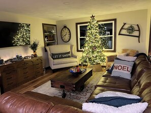 Una sala acogedora con un árbol de Navidad, un sofá, un sillón, una mesa de centro y un reloj en la pared.
