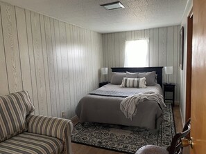 Un dormitorio con una cama, mesitas de noche, una silla y una alfombra estampada.