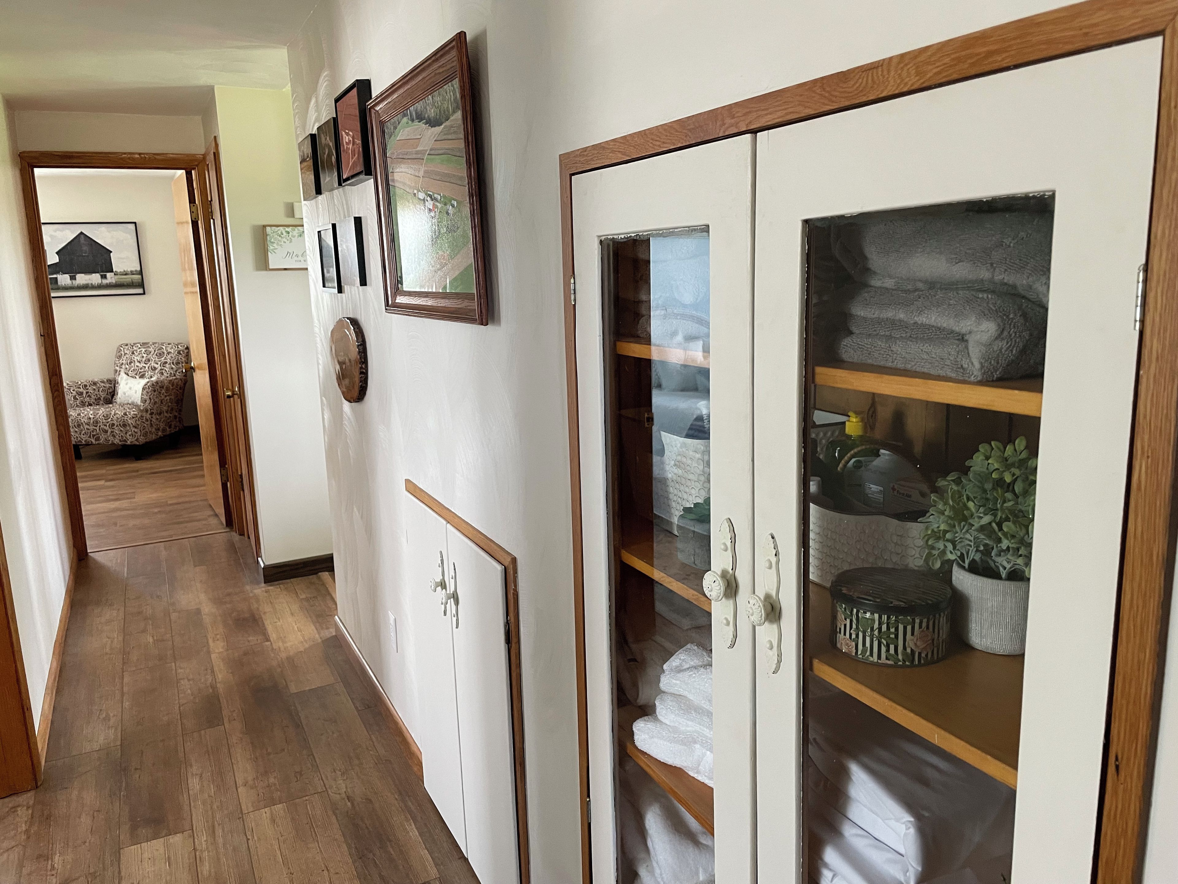 A hallway with a wooden floor, a wardrobe with a glass door, and a chair.