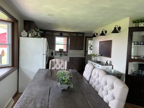 A kitchen with a dining table, chairs, a refrigerator, cabinets, and a window.