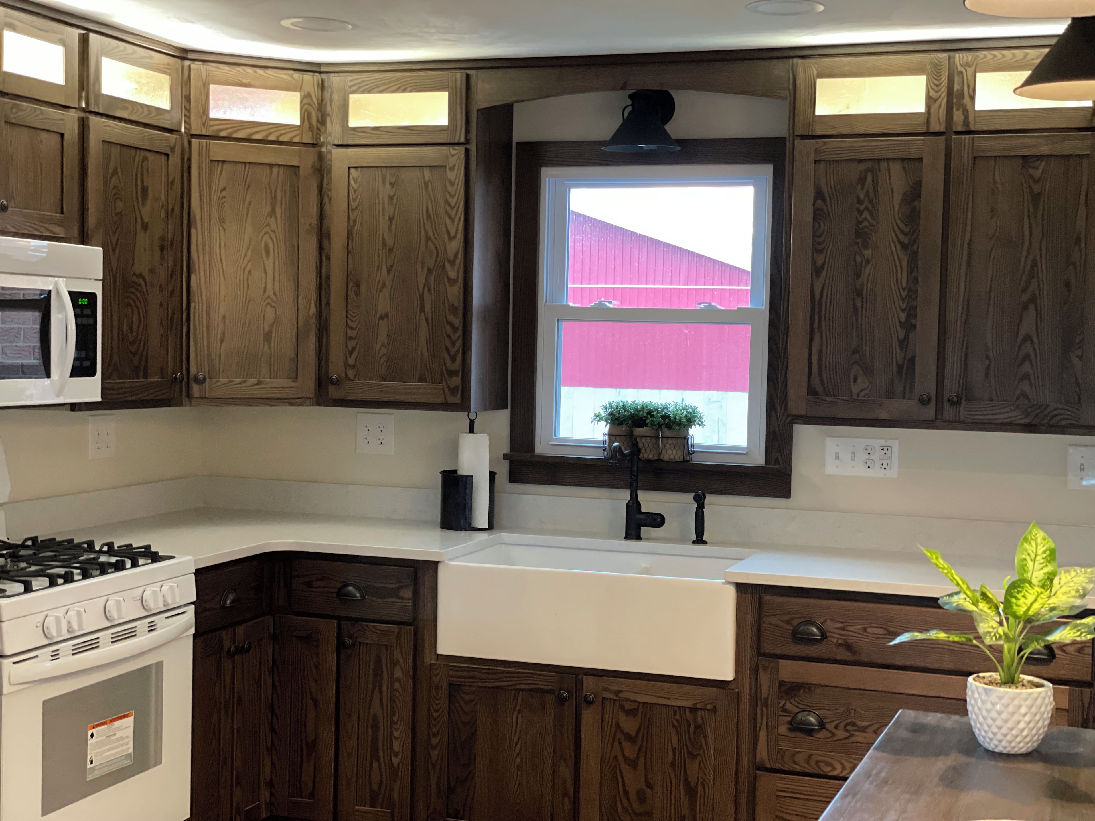A kitchen with wooden cabinets, a microwave, a stove, a sink, and a window with a view of a red building.